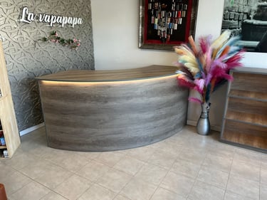 Curved wood-finish reception desk with warm LED lighting and colorful pampas grass decor.