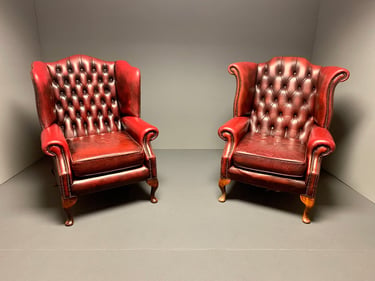 Two vintage, orang leather armchairs with tufted backs sit side by side in a minimalist, neutral-colored room. 