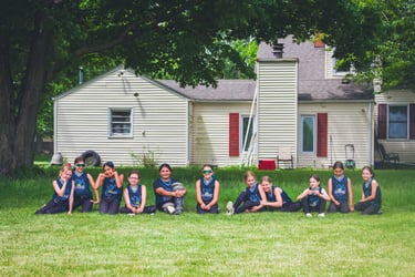 Photo of 10u Dragons sitting in grass in front of white house
