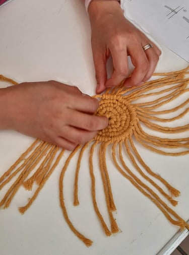 manos tejiendo un posavaso de macramé color amarillo en forma de espiral