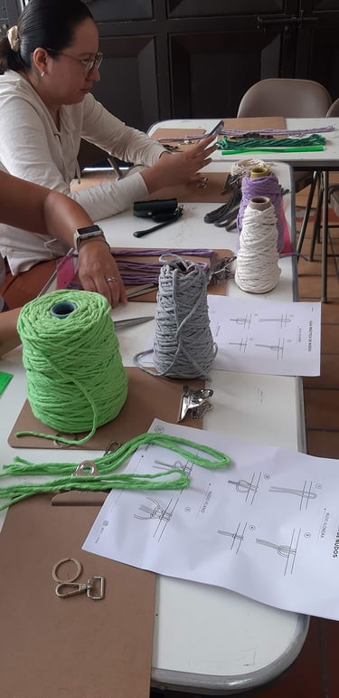 mesa de trabajo con cordones de macramé de colores, hojas con instrucciones y una persona de fondo