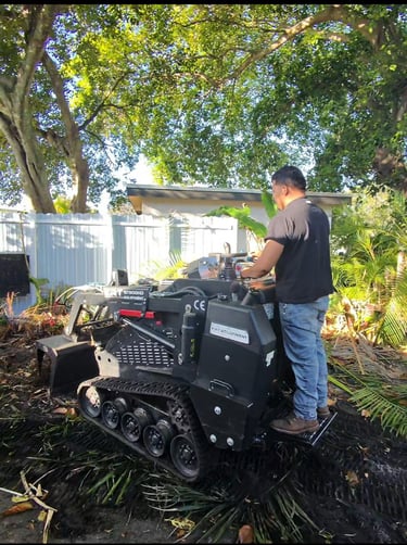 A man operating a black KRT ST900HD mini track loader for backyard landscaping and debris removal.