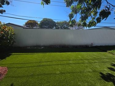 Freshly installed green artificial grass lawn in a residential backyard with a white privacy fence.