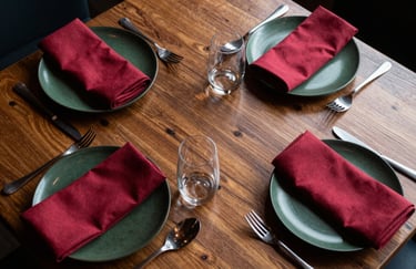 A top-down professional shot of an artisanal dining table in a North American restaurant, featuring dark forest green plates and crimson napkins.