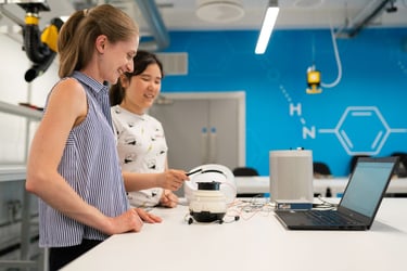 Two female engineering students working on a robotics project with a laptop in a modern science laboratory.