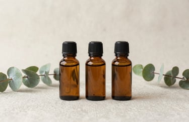 Minimalist photo of three glass bottles of essential oils arranged neatly on a textured soft cream linen cloth, natural eucalyptus green stems nearby.