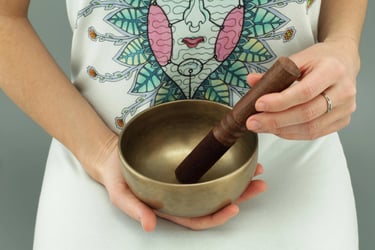 Une personne à genoux, qui effectue un soin de sonothérapie avec un bol tibétain dans les mains.