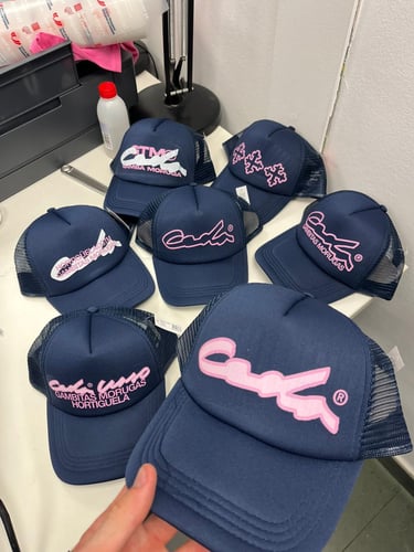Collection of navy blue Gambitas Morugas trucker hats with pink embroidered logos and mesh backing.