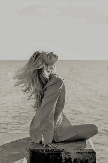 Orlane in an oversized blazer posing by sea with windblown hair in a black and white fashion shot.