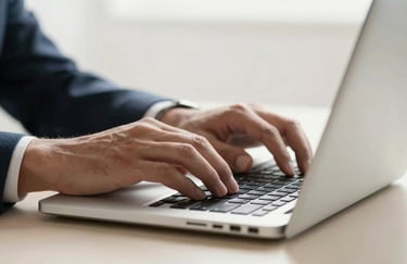 A close-up shot of professional hands typing on a high-end laptop in a bright North American / International office, with a soft off-white background.