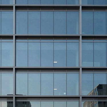 A minimalist architectural shot of a North American / US modern office building's glass facade reflecting a clear sky, dominated by blue and gray tones.