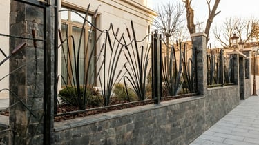 Custom wrought iron fence with cattail design on a modern stone wall for luxury property security.
