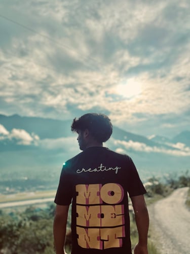A man in a Mountfit t-shirt looks out over a scenic mountain valley under a bright, cloudy sky.