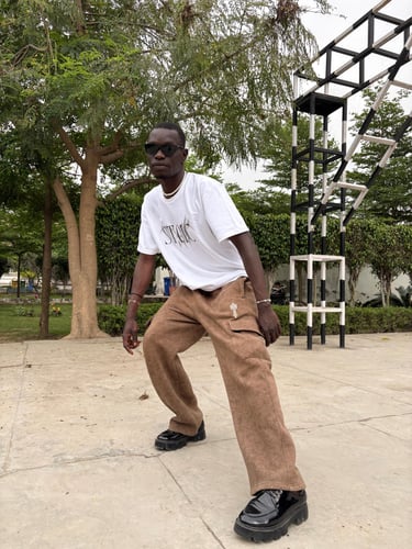 A man in a mountfit white graphic t-shirt and brown cargo pants posing in a park with sunglasses.
