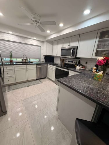 Modern kitchen with white shaker cabinets, dark granite countertops, and marble tile flooring.