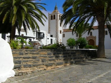 Historic white church in Betancuria, Fuerteventura, framed by palm trees and stone steps.