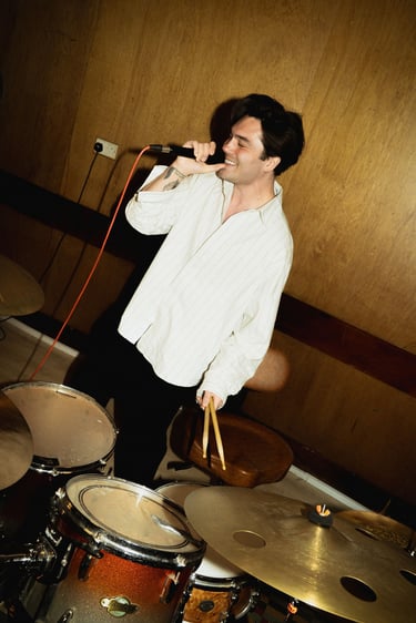 George Shelley singing in front of a drum kit