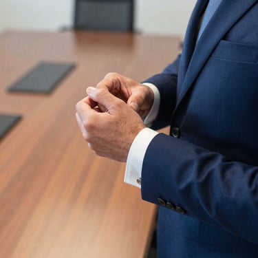 A close-up photograph of a professional in a sharp navy suit adjusting a silver cufflink in a well-lit North American boardroom. The focus is on the precision of movement, exuding an aura of discretion.