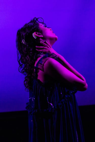 A brown woman with flowing hair and hearing aids bathed in purple light
