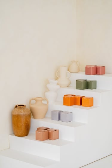 Handcrafted ceramic vases and colorful candle boxes displayed on a minimalist white staircase.