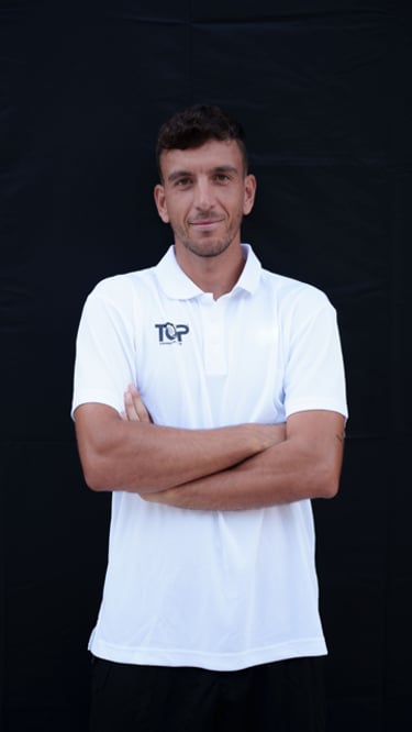 Professional padel coach in a white TOP Training Padel Club shirt posing with crossed arms.