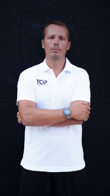 Professional male fitness trainer in a white polo shirt with arms crossed against a black background.