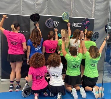 A group of female padel players in colorful jerseys posing with rackets at an indoor court tournament.