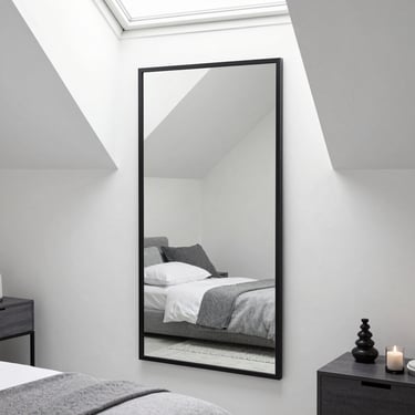 Grand miroir noir posé au sol reflétant une chambre épurée.