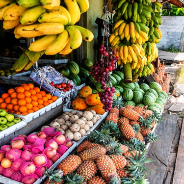 A vibrant market stall overflowing with tropical fruits, including yellow bananas, fresh pineapples, and green watermelons.