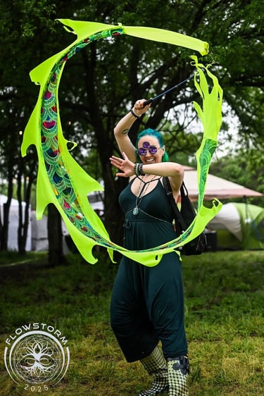 A woman with teal hair and third eye covering sunglasses spins a neon green dragon kite in a circle
