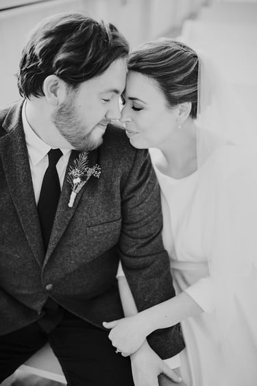 Black and white portrait of a bride and groom touching foreheads in a romantic wedding moment.