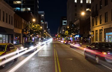 A vibrant long-exposure photograph of a North American city street at night, capturing light trails from cars moving with speed.