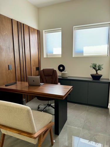 Modern home office with a wooden desk, leather chair, laptop, and bonsai tree.