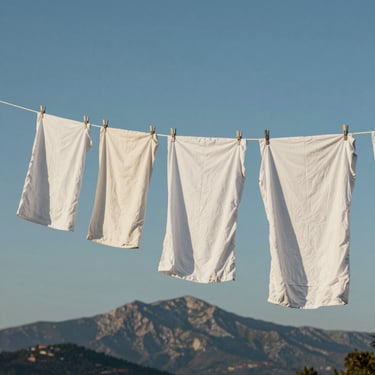 Fresh white laundry hanging on a line against a blue sky with the silhouette of Corsican mountains in the distance, soft lighting, Southern European / Corsica.