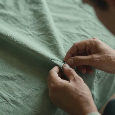 Close-up of a specialist's hands inspecting the stitching of a high-quality tablecloth, soft and focused lighting, muted green tones, Southern European / Corsica.