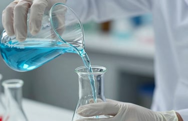 Close up of hands in nitrile gloves pouring a blue chemical solution from a beaker into a volumetric flask. High precision and sophisticated professional atmosphere.
