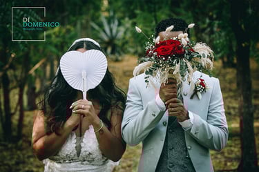 Mariés cachant leurs visages avec un éventail en forme de cœur et un bouquet de roses rouges lors d’une séance photo de maria