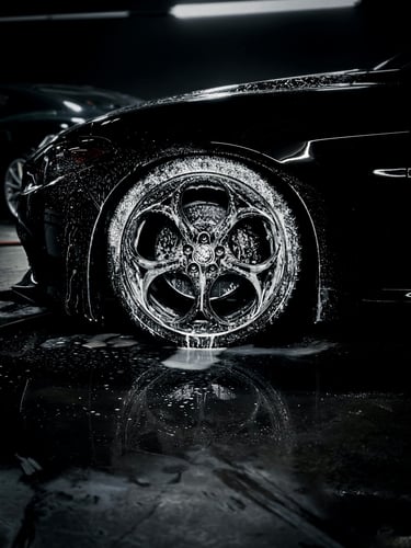 Professional car detailing of a black luxury car with soapy foam on custom alloy wheels and tires.