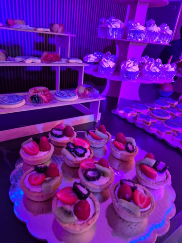 Mini tartaletas de fruta con fresas y kiwi presentadas en una mesa de postres con iluminación de fie