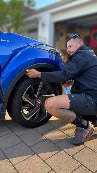 A technician inspecting a blue cars wheel arch after paintless dent removal.