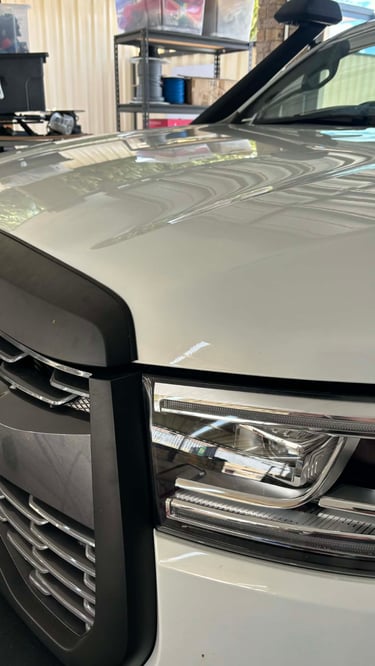 Close-up of a white 4x4 vehicle's bonnet repair using paintless dent removal.