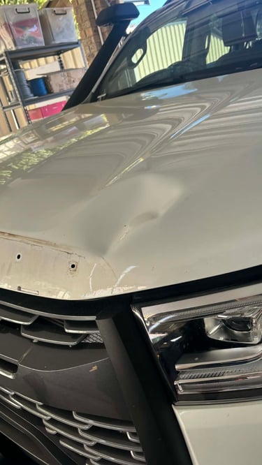 Close-up of a large dent on the white hood of a modern vehicle requiring paintless dent removal.