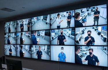A high-end security monitoring room with multiple flat screens displaying surveillance feeds. The lighting is soft pale blue, projecting an image of unwavering reliability and sophisticated monitoring expertise.