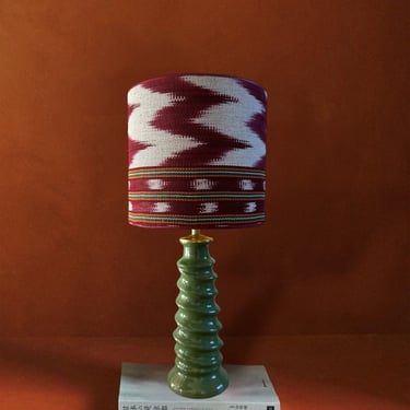 Green ceramic table lamp with a patterned ikat lampshade on a book against an orange background.