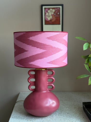 Pink ceramic table lamp with a patterned ikat lampshade on a stone tabletop.