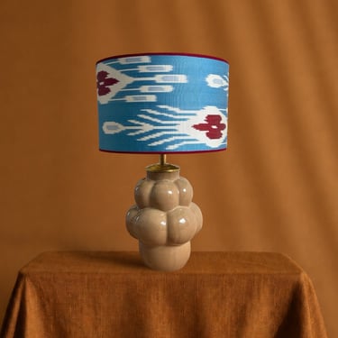 A ceramic table lamp with a blue ikat patterned lampshade on a textured brown background.