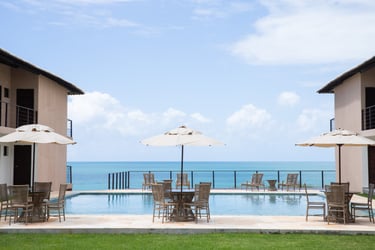 Luxury beachfront resort pool with patio furniture and umbrellas overlooking the blue ocean.