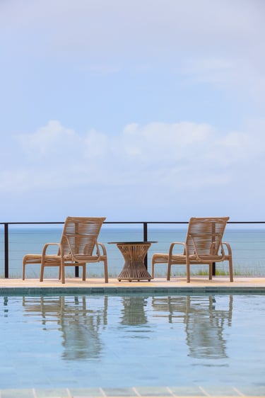 Woven wicker lounge chairs and side table by a luxury infinity pool overlooking the ocean.