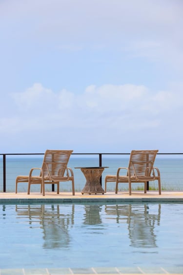 Modern wicker patio lounge chairs and side table on a luxury poolside deck with ocean views.