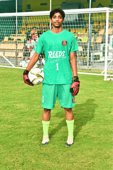 Young goalkeeper in a green Reeds Football Club kit holding a soccer ball on a grass field.